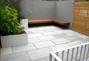 Courtyard in Herne Hill SE24 with a grey Indian sandstone paving area, in-built hardwood bench, grey rendered corner wall, contemporary planters and venetian trellis boundaries